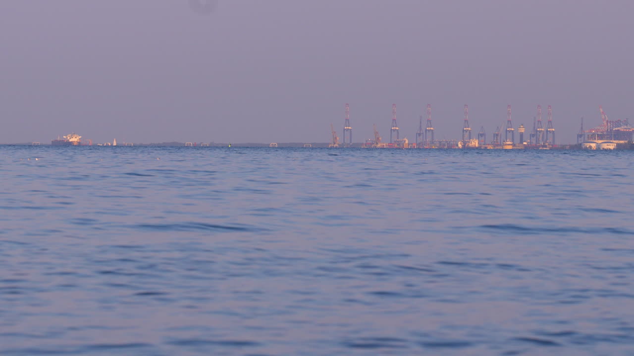 Wide view of sea with industrial port cranes on horizon