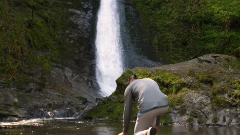 Young-bearded-man-approaching-a-small-lake-with-waterfall-and-washing-his-face