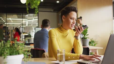 Happy-caucasian-businesswoman-sitting-at-table-and-using-smartphone-at-office