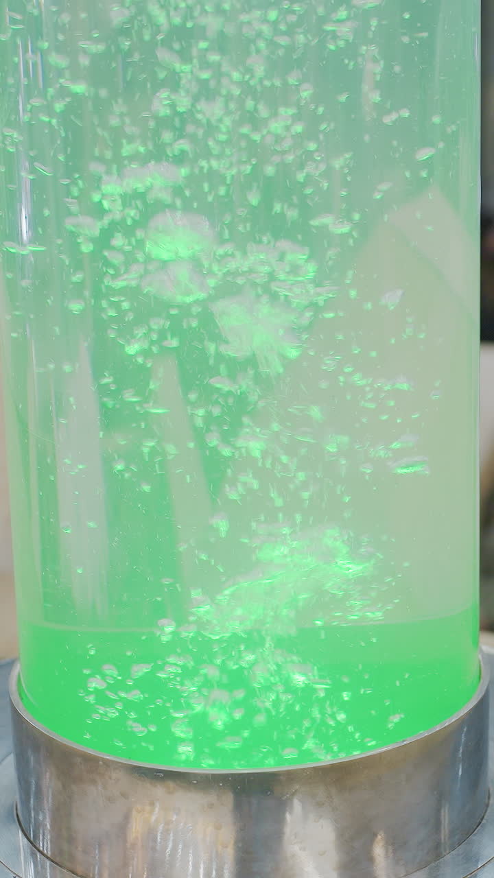 Beautiful Christmas decorations in mall with glowing Christmas lights, festive ornaments, and large cylindrical water feature in center, with blurred people in background