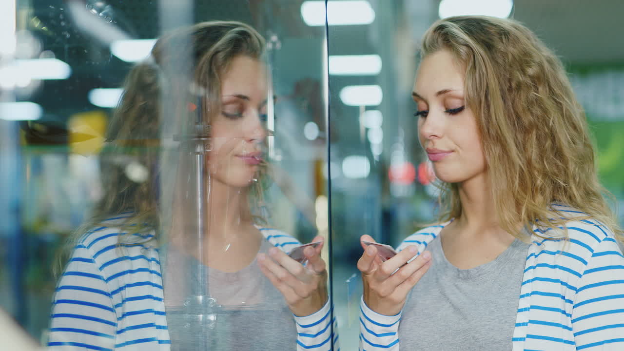 una joven triste se para en el escaparate en manos de su tarjeta de pago, está molesta por un video de alta definición