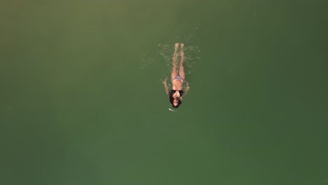 aerial top down shot tracking female in bikini relaxing swimming in beautiful green ocean water surface