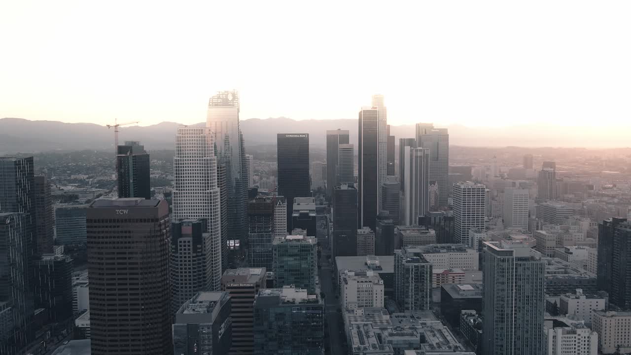 un joven adulto se para en un rascacielos en el centro de los ángeles al amanecer levantando las manos mientras un dron pasa