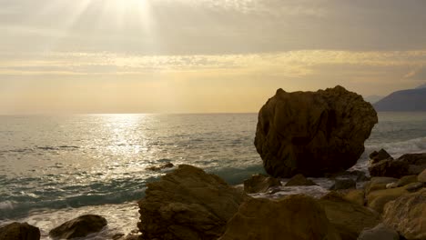 Meereslandschaft-In-Der-Dämmerung-Mit-Sonnenstrahlen-Auf-Der-Meeresoberfläche,-Die-Durch-Einen-Felsigen-Strand-Im-Mittelmeer-Gesehen-Werden