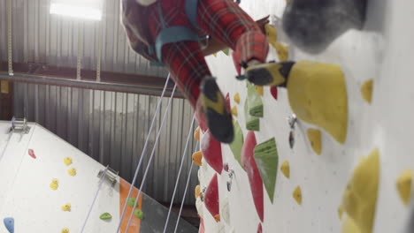 un joven escalador en forma escala una ruta de retenciones amarillas, haciendo su camino hasta la pared en un gimnasio de escalada