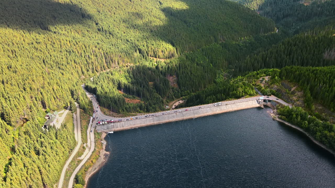 Aerial drone view of the Oasa Dam in Romania. Carpathian mountains, hills with lush forest, multiple cars