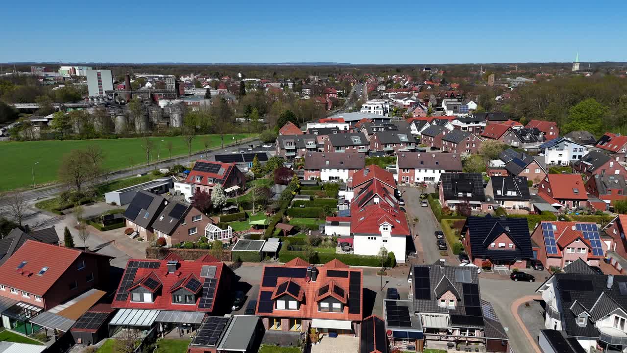 Sunny day in modern housing area with semi-detached houses and solar panels on roof. Aerial wide shot.Cars in street near farm fields. Factory building in distance.