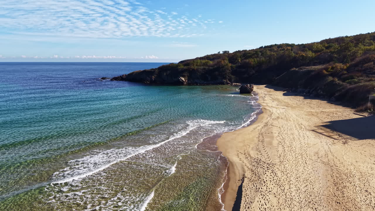 Lugna vågor smeker försiktigt sandstranden under en klarblå himmel under en stillsam eftermiddag vid havet