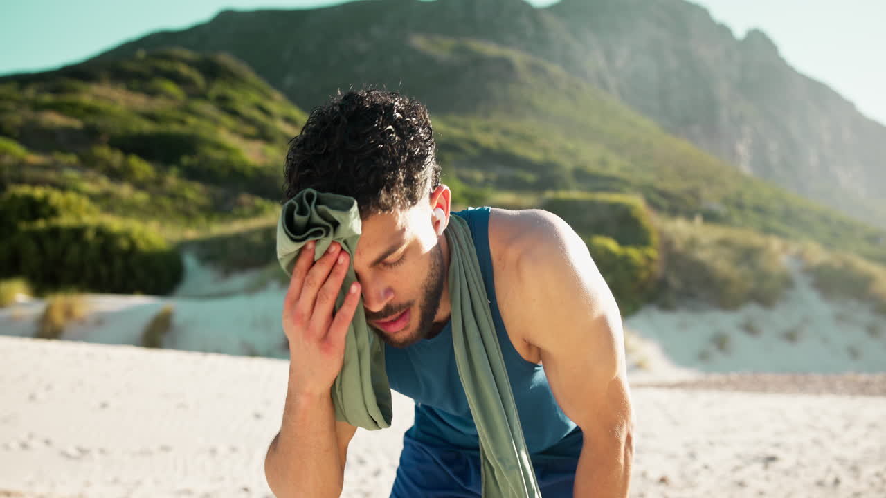 Uomo stanco che si asciuga il sudore con un asciugamano dopo un allenamento all'aperto in spiaggia