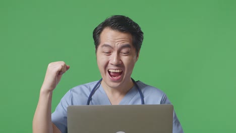 close up of asian male doctor with stethoscope looking at a laptop and celebrating the succeed on green screen background in the hospital