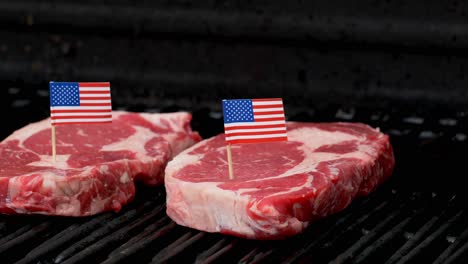 Zwei-Saftige-Rib-Eye-Steaks-Sitzen-Auf-Dem-Grill-Und-Kochen-Mit-Zwei-Winzigen-Zähnen-Der-Amerikanischen-Flagge,-Die-In-Sie-Gestochen-Werden