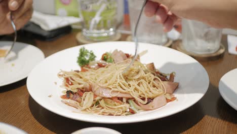 close up view to hand using fork to eat spicy spaghetti with sausage in white plate