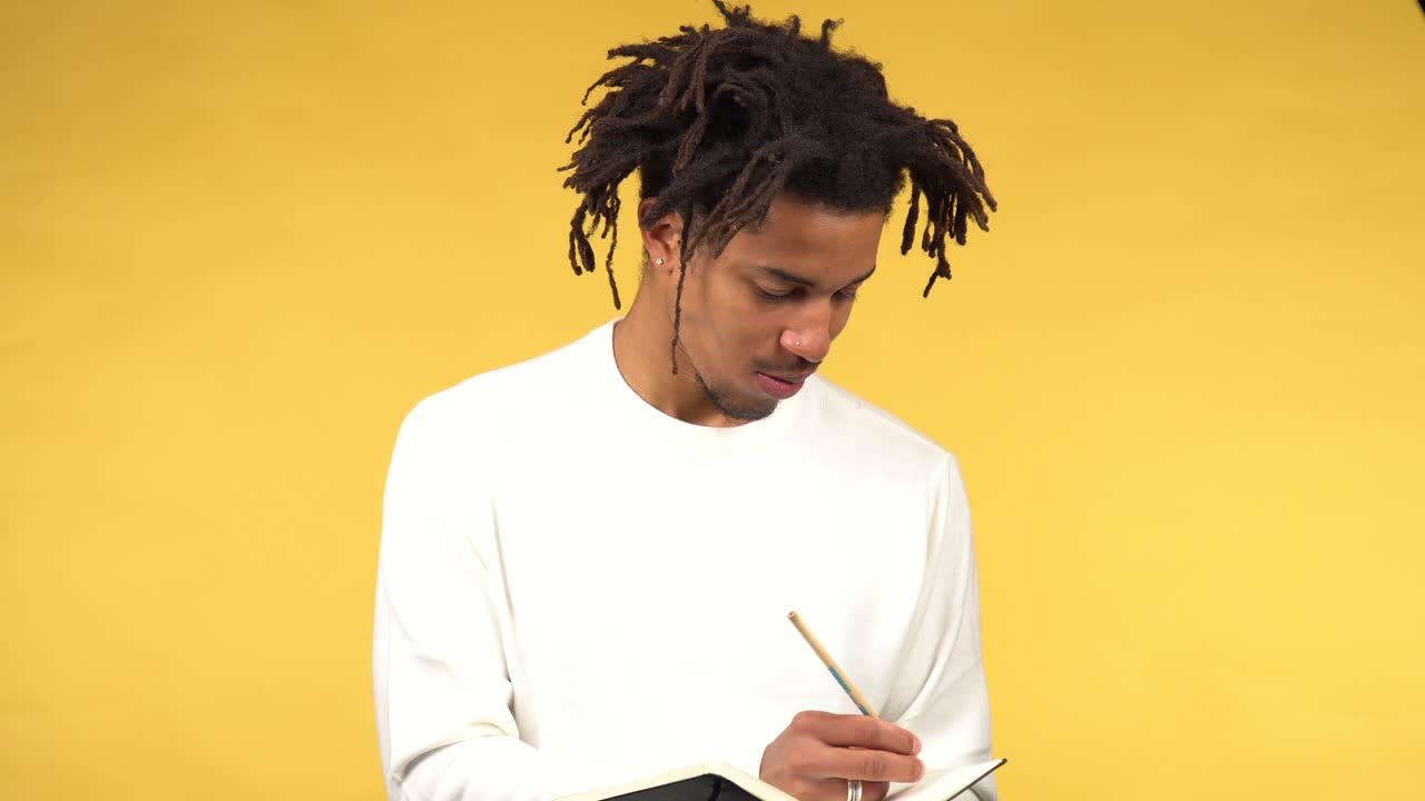 Thoughtful afro american student write his ideas in a notebook, yellow background