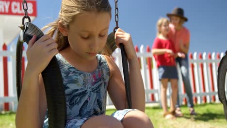 Upset-girl-sitting-on-a-swing-while-friends-talking-in-the-background-4k