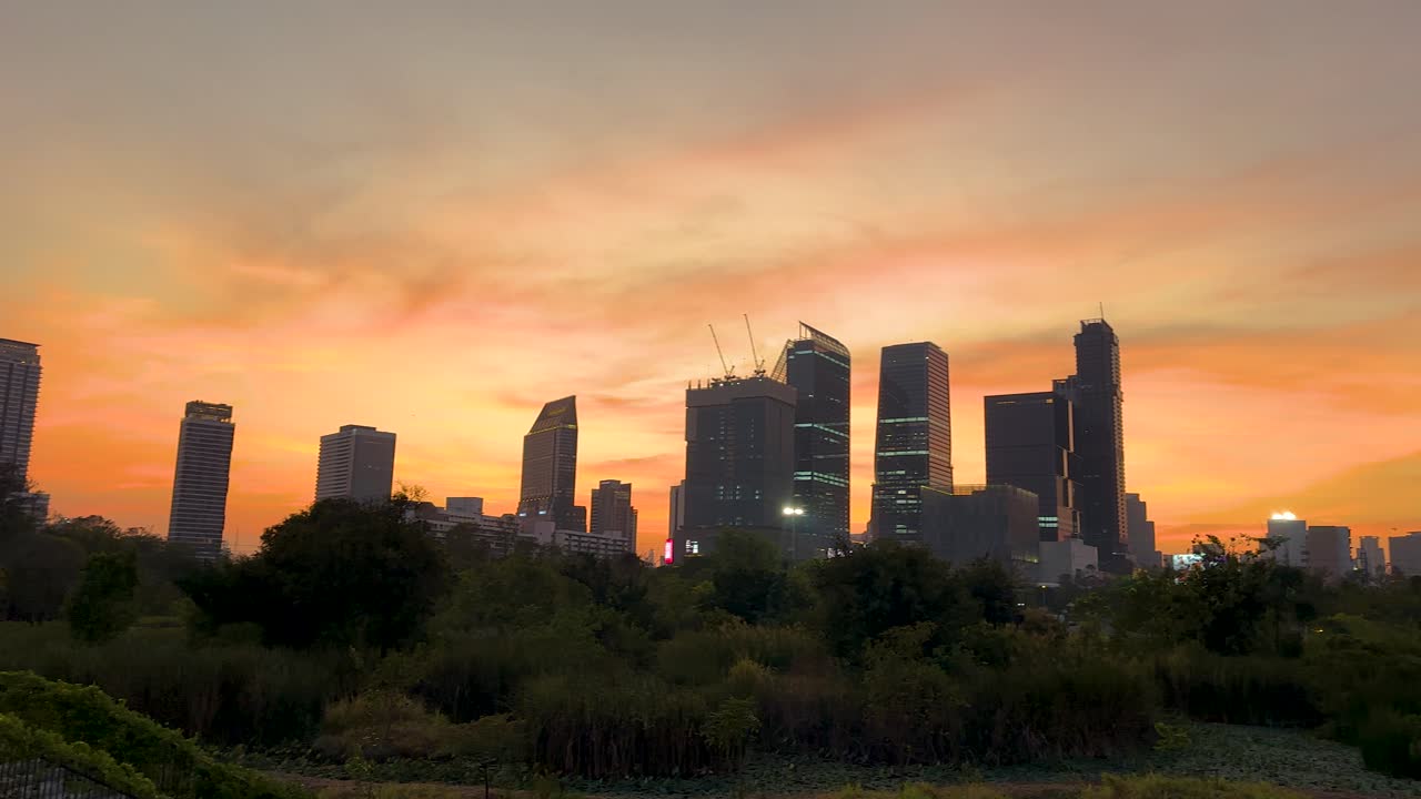 Um pôr do sol sereno projeta tons quentes sobre o horizonte de Bangkok, visto da exuberante vegetação do Parque Benjakitti