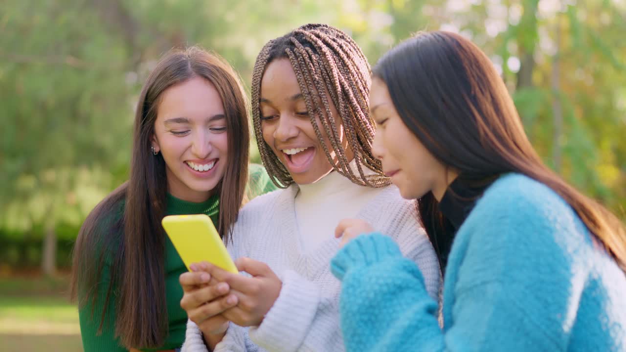 Three diverse friends laughing and looking at a smartphone in a park