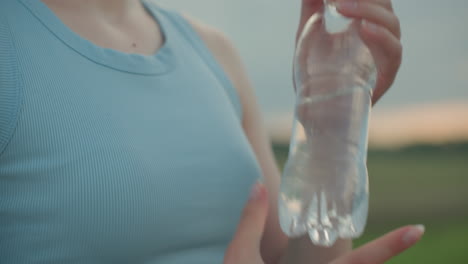 close up of hands closing cap on water bottle after countryside stroll under dramatic sky at sunset capturing hydration moment and detailed plastic twist gesture against blurred road