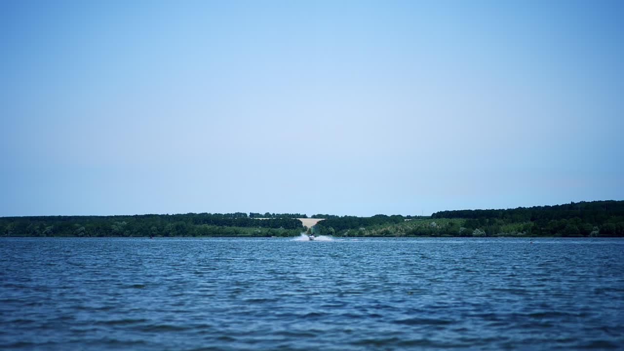 Beautiful blue river on sunny summer day with a speed boat approaching camera. Green waterfront and clear sky at backdrop.