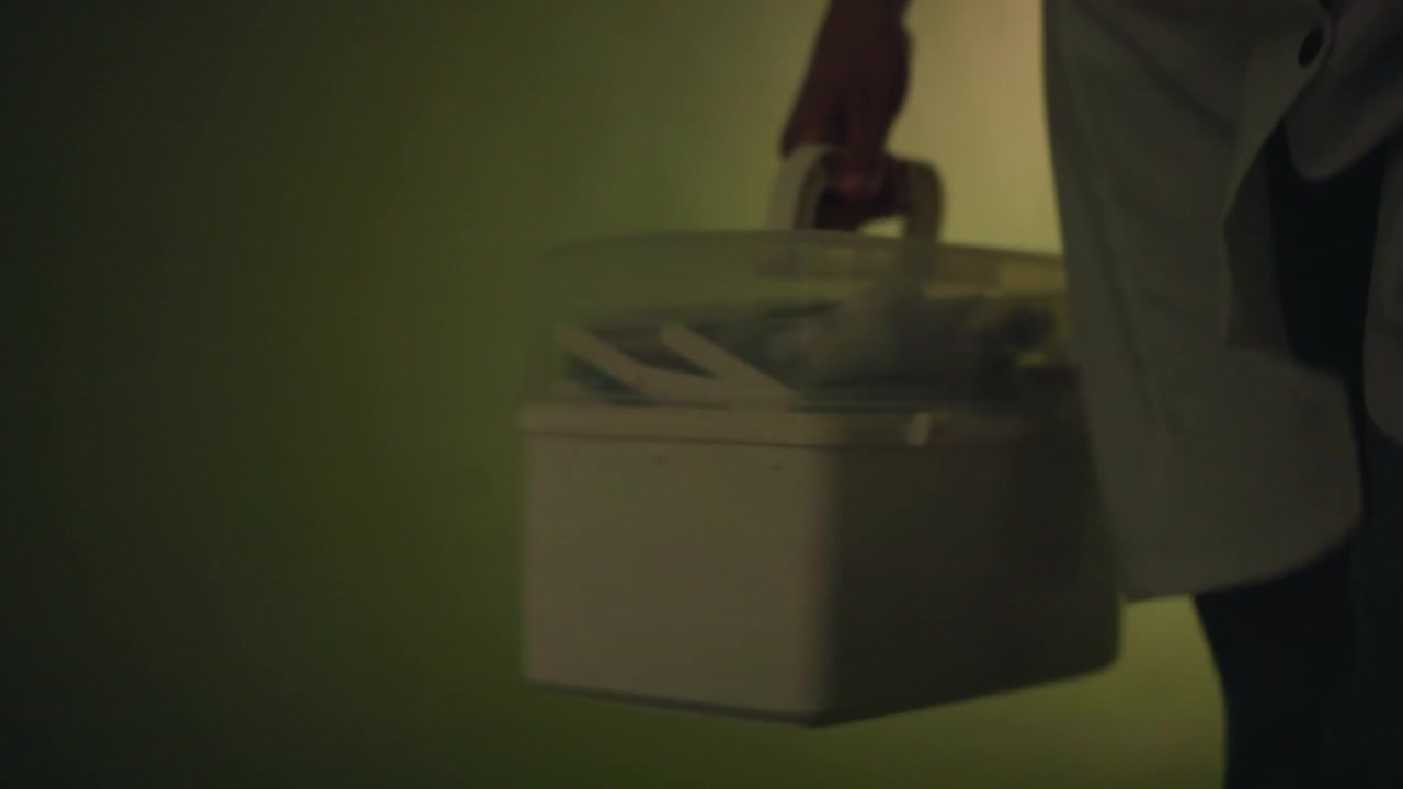 Infermiera che consegna un contenitore medico refrigerato durante una visita domiciliare, mano ferma sull'impugnatura, illuminazione calda del corridoio e porta d'ingresso residenziale, passo compassionevole e assistenza di routine per la consegna di medicine e campioni.