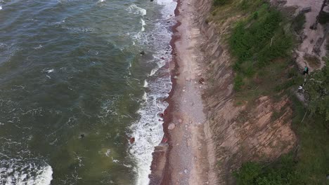 overhead drone views showcase the rugged charm of a high cliff coast in lithuania's baltic sea, where powerful waves meet the enchanting green sea, painted with moody colors