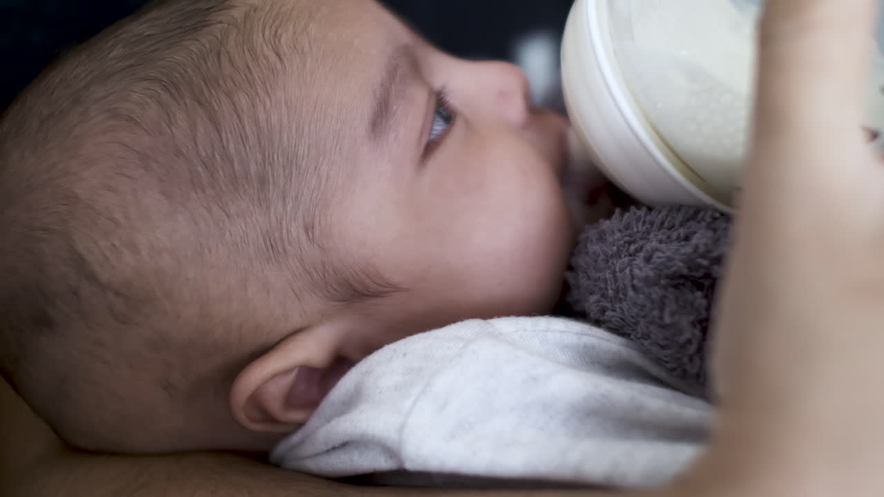 niño indio de 2 meses bebiendo leche materna del biberón seguido de limpiarse la boca con una toalla