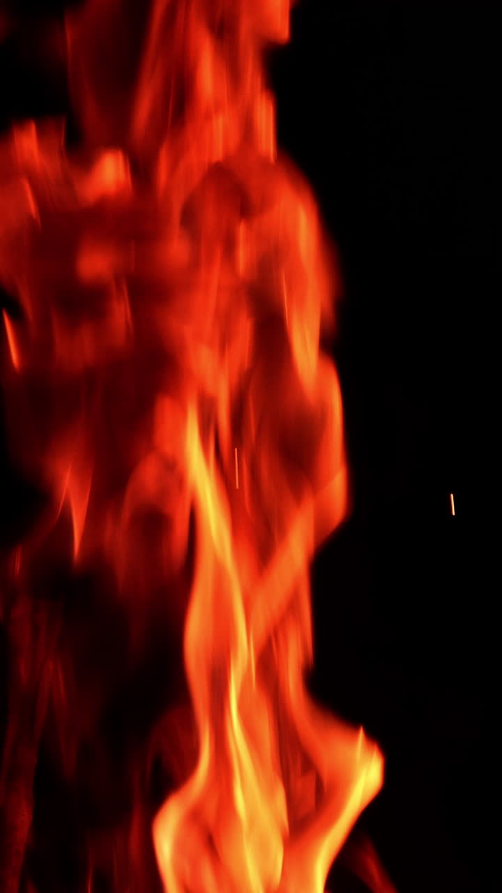 Beautiful red fire burning at night. Little sparkles fly up from the flame. Close up. Vertical video