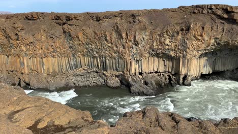 basalt rocks next to majestic waterfall aldeyjarfoss in the highlands of iceland on a cold and windy day