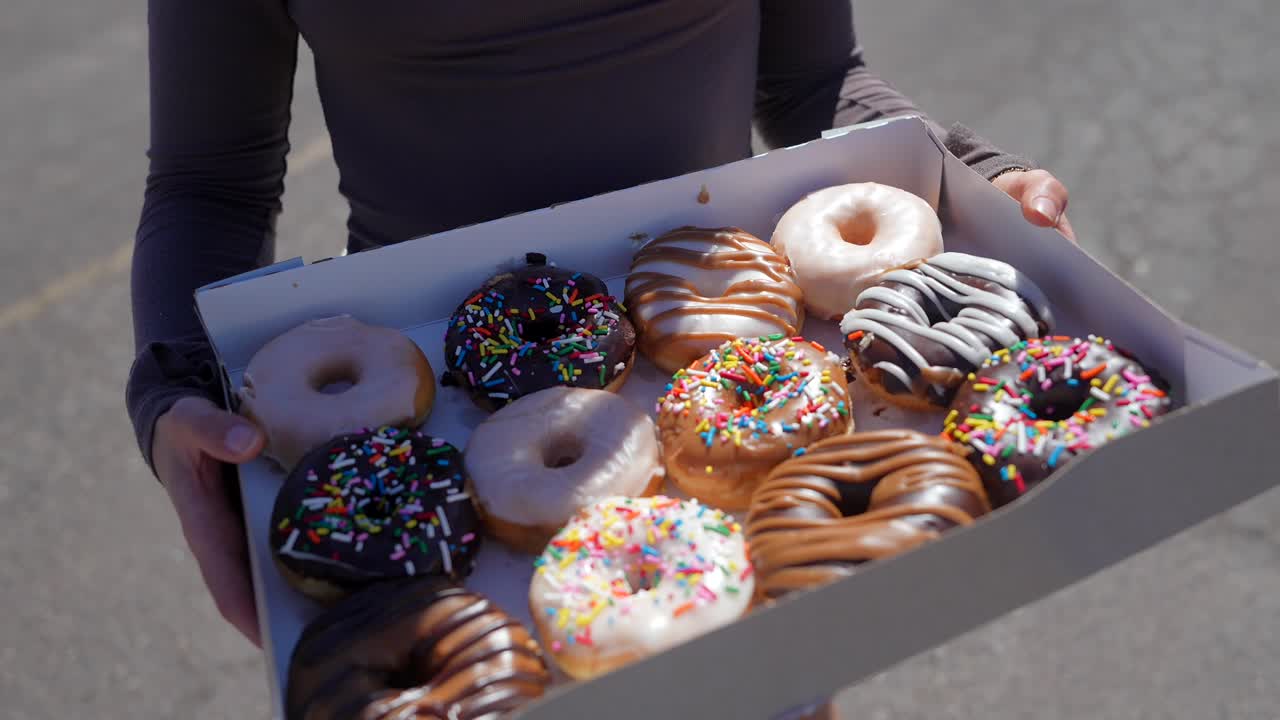 Jovem Mulher Sorrindo e Segurando uma Caixa de Donuts ao Ar Livre