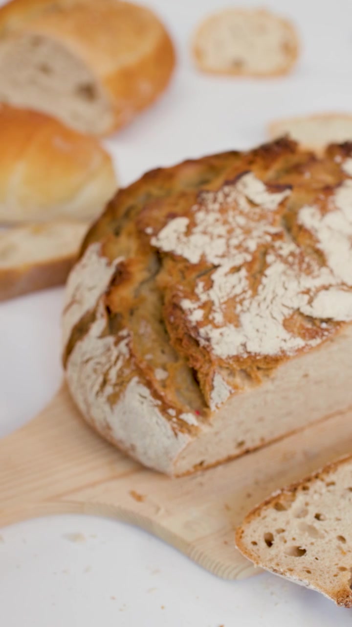 Close-up of hands tearing crusty whole wheat bread on a bright white studio background.