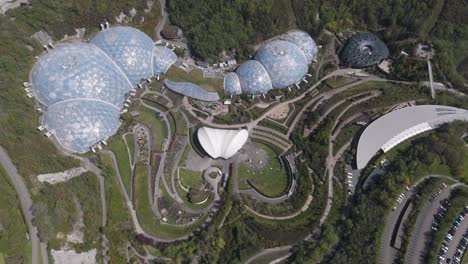 expansive aerial panorama of eden project glass biomes nested in spiral gardens amid forested quarry, symbolising sustainable design, climate education and ecological diversity