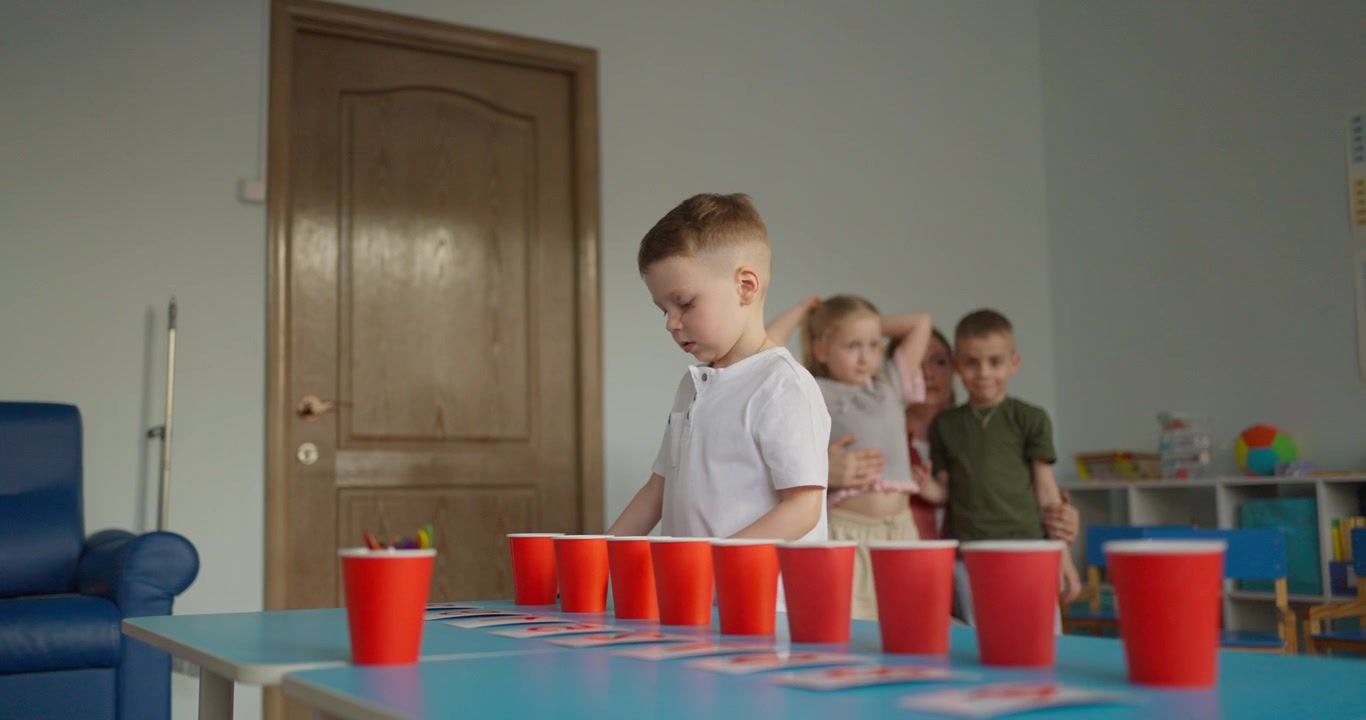 Young Boy Playing Educational Game with Red Cups and Cards in Classroom