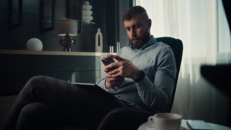 concentrated professional stock exchange broker using smartphone, monitoring real-time stocks and exchange market charts. successful investment agent working in cozy office of financial agency.