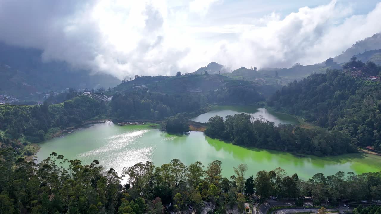 Beautiful aerial shot of a crater lake with shimmering emerald and turquoise water, encircled by lush vegetation and rolling hills. A tranquil and colorful natural wonder in a cool mountain landscape