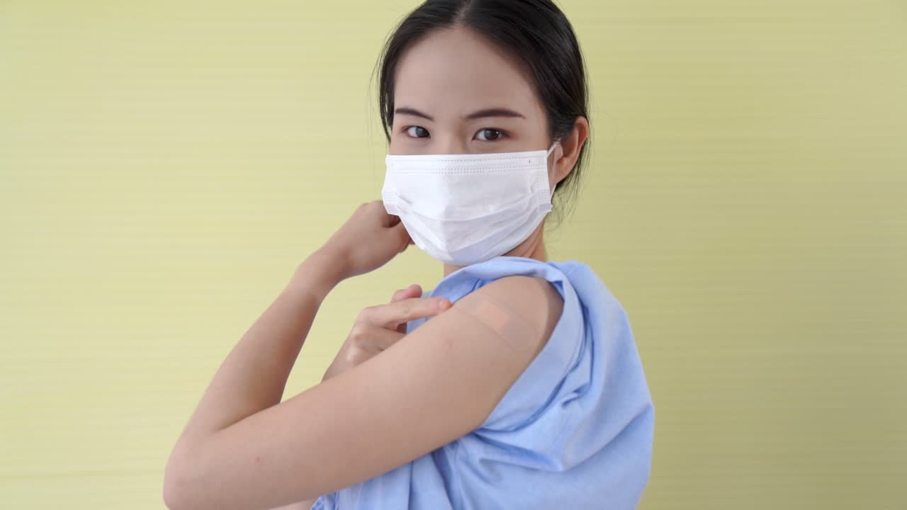 Young Asian woman showing COVID-19 vaccine bandage merrily
