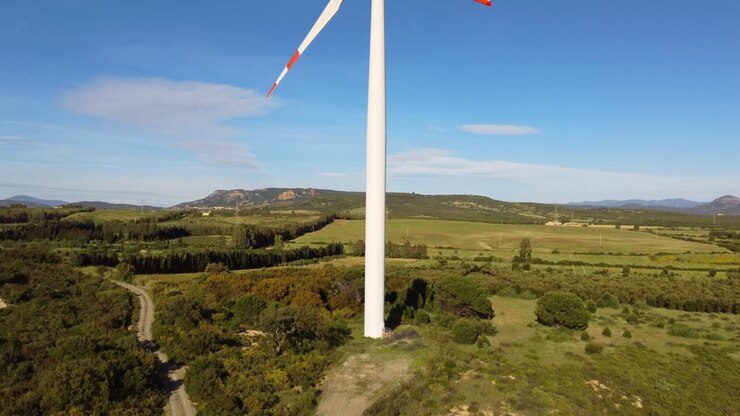 Wind turbine in rural landscape, aerial rising reveals blades, sunny day