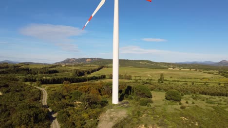 Wind-turbine-in-rural-landscape,-aerial-rising-reveals-blades,-sunny-day