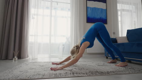 young woman meditating sitting on carpet and doing splits stretching doing yoga blue sportswear light room at home in the morning. woman practicing yoga at home