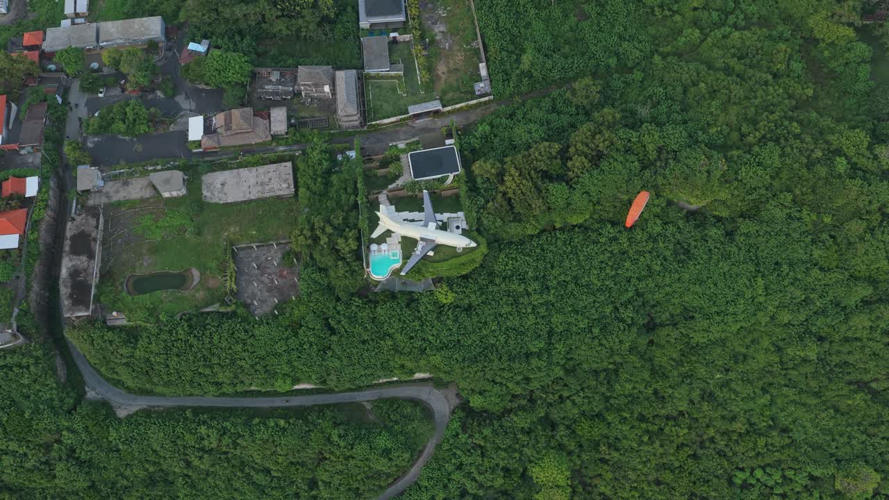 緑豊かな景観の上空に、飛行機型ヴィラとパラグライダーの空撮