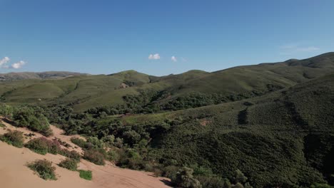 Aerial-push-in-above-deep-valley-filled-with-half-sand-and-half-green-shrubbery