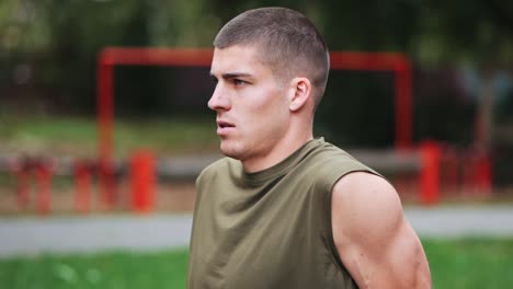 Focused-young-athletic-man-doing-push-ups-at-red-sports-equipment-in-facility-park,-tracking-shot