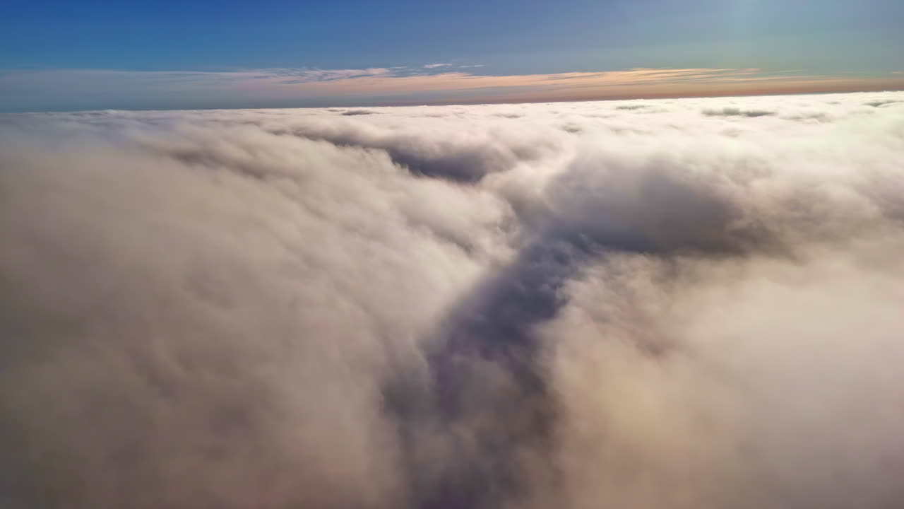 Drone pulls back and shifts right above a dense cloud layer at dawn