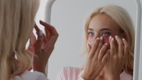 mujer aplicando parches en los ojos frente a un espejo