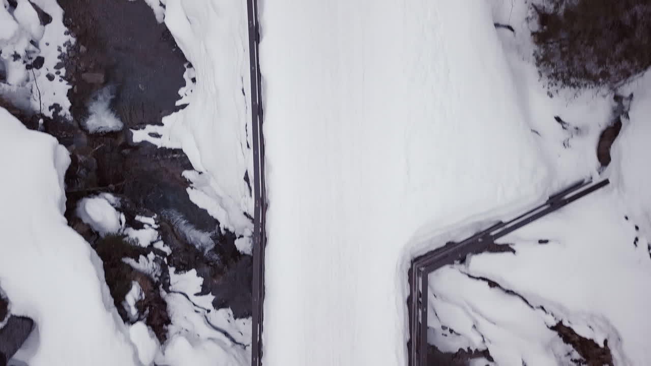 Aerial view of a small bridge over a creek in a snowy valley in the alps, Kleinwalsertal,Austria Drone moving forward and looking down