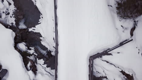 Aerial-view-of-a-small-bridge-over-a-creek-in-a-snowy-valley-in-the-alps,-Kleinwalsertal,Austria-Drone-moving-forward-and-looking-down