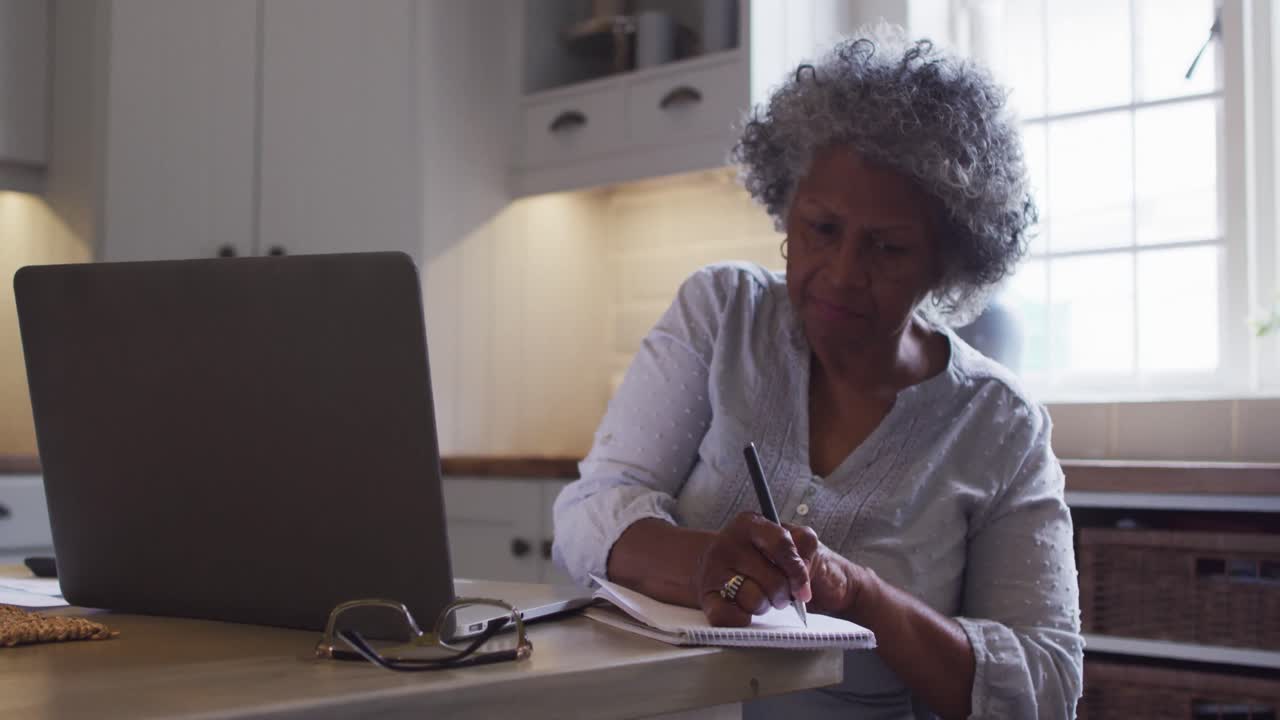 Senior african american woman using laptop and taking notes at home