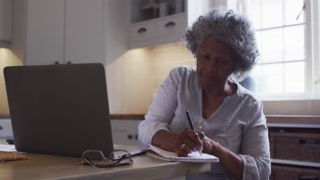 senior african american woman using laptop and taking notes at home