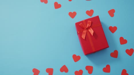 Multiple-red-paper-hearts-and-red-present-at-valentine's-day-on-blue-background