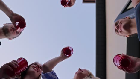 bottom view of a happy group of friends clinking red glasses during their party and relaxation in the courtyard of a country house