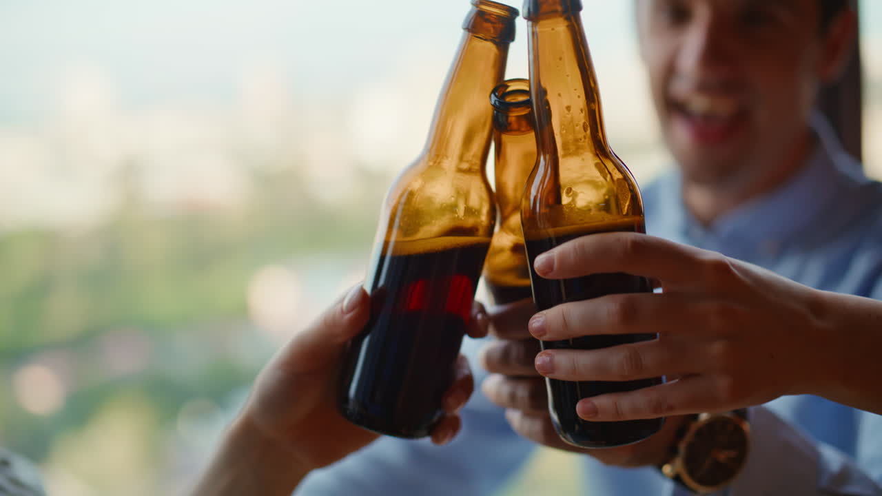 Amici rilassati che brindano con delle birre chiacchierando in un appartamento con vista sulla città, primo piano