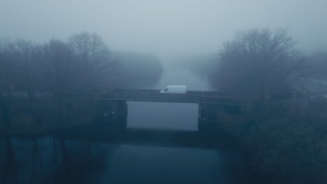 Side-shot-of-car-crossing-bridge-with-blanket-of-fog-during-early-moody-morning-hours